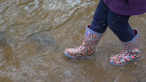 young child walking and splashing water in welly boots