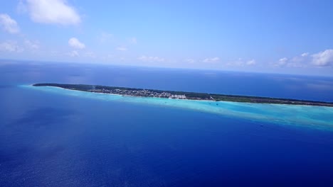 vista aérea a gran altura de una isla cubierta de palmeras en las maldivas mientras el color del mar va de turquesa a azul oscuro