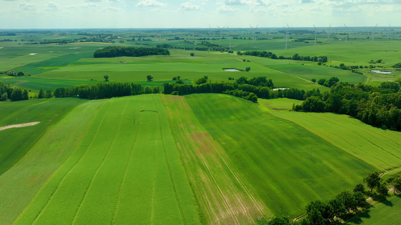 Aerial view of vast green farmlands with wind turbines in the distance