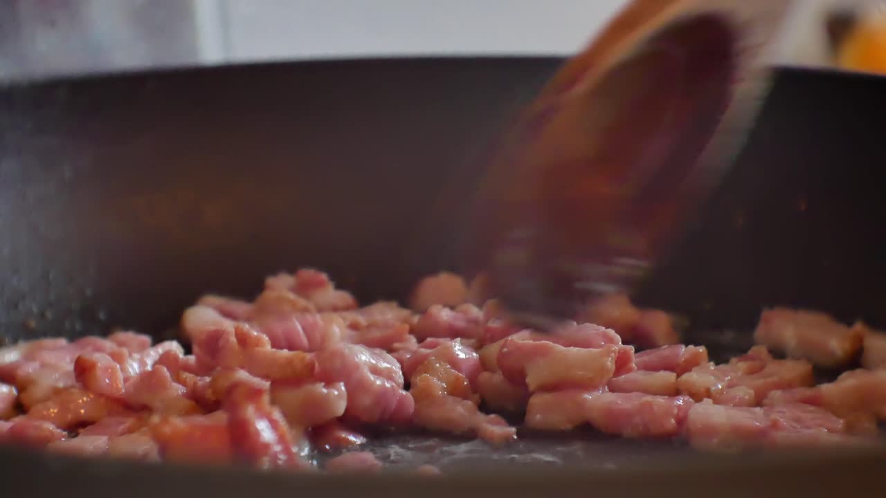뜨거운 김이 나는 난로 위에서 맛있는 먹을 수 있는 요리를 준비하기 위해 바삭바삭하고 짠맛이 나고 기름기가 많고 튀긴 베이컨 조각을 닫습니다