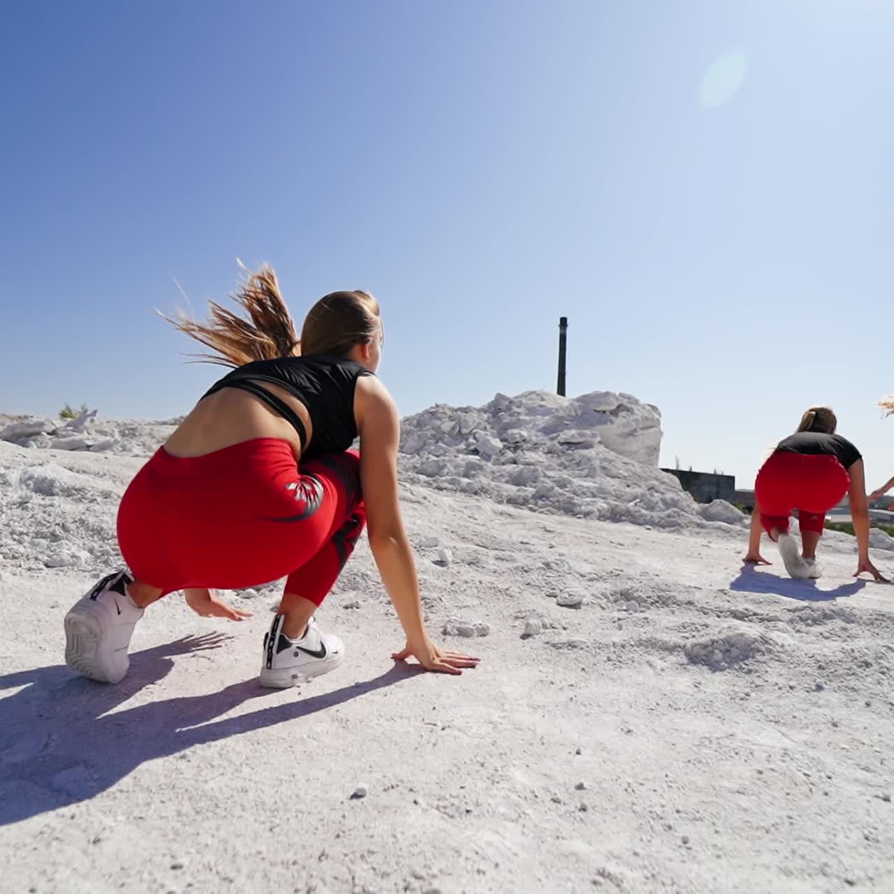 Three girls in black tops and red pants dance outdoors. Dance group performs in the industrial area. Low angle view