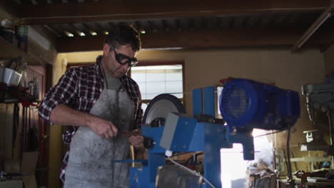 caucasian male knife maker in workshop wearing glasses and using saw