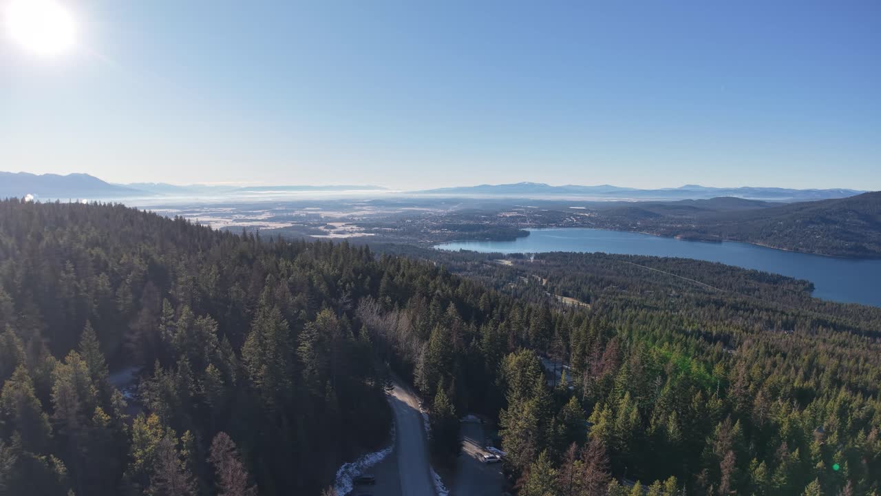 Pemandangan udara lereng bukit berhutan dan danau-danau jauh di bawah langit biru cerah dekat Whitefish, Montana