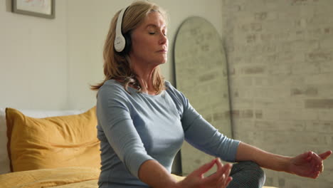 senior woman meditating with headphones at home, enjoying peaceful music
