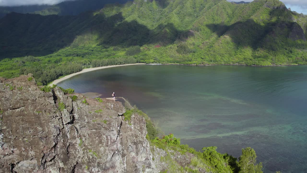 la pareja de viajeros se para en la roca del león agachada en hawaii, vista de drones de la bahía de kahana