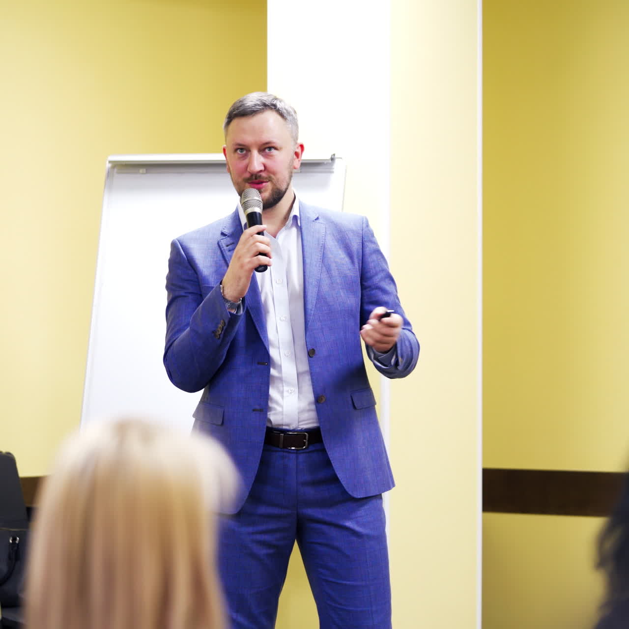 Confident executive manager with microphone speaking at meeting for the public. Businessman in blue suit gives advices for audience on business forum.