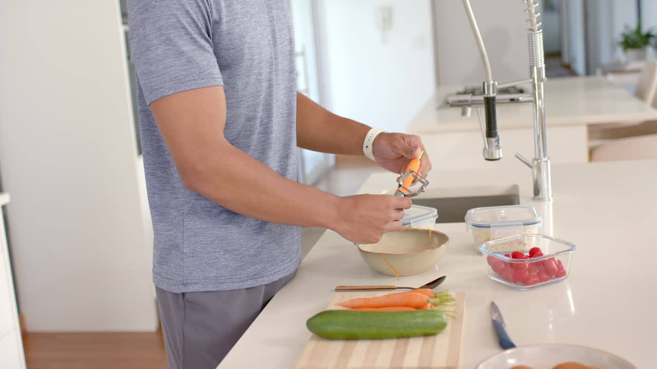 Un uomo prende e sbuccia una carota sopra una ciotola mentre prepara i contenitori per i pasti sul bancone.