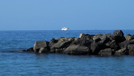 Muelle-De-Piedra-En-La-Playa-De-Playa-De-Las-Américas,-Día-Soleado-De-Verano,-Océano-Atlántico-Tranquilo-En-El-Fondo,-Ferry-Turístico-Distante,-Toma-De-Mano-Mediana