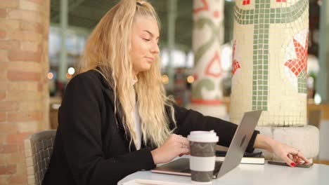 woman talking on smartphone while working with laptop in cafe