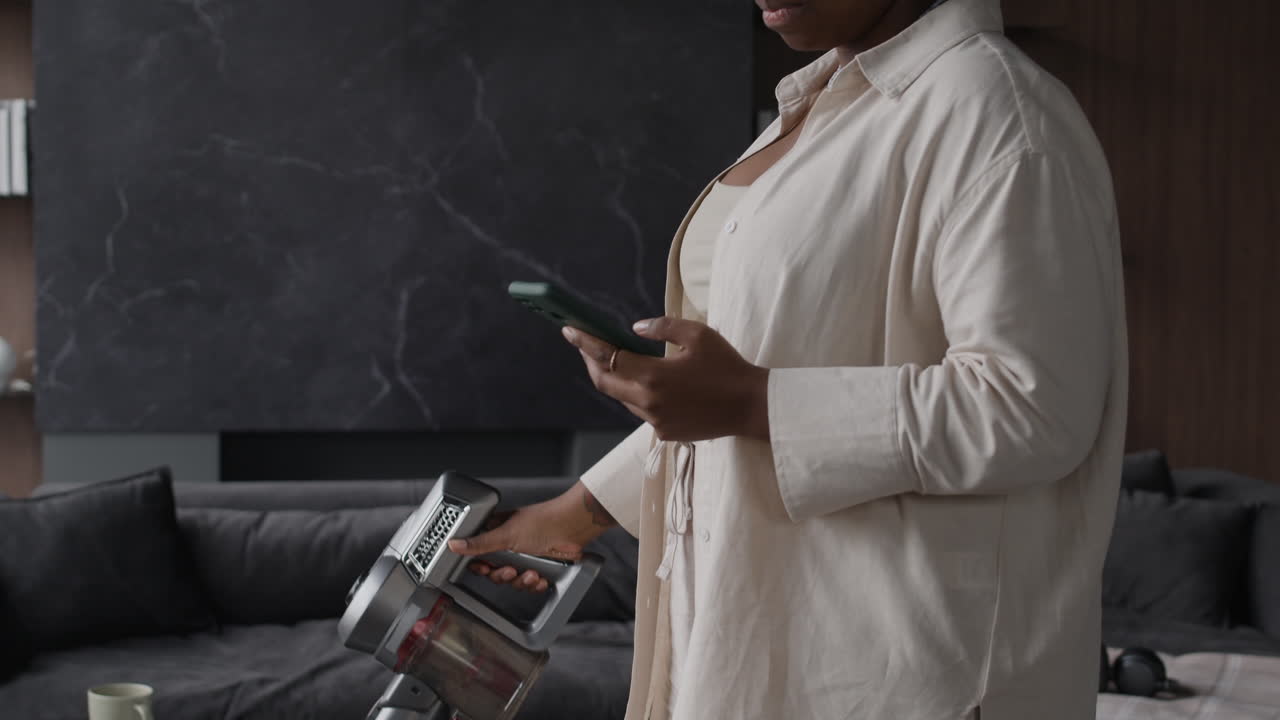 Woman Using Vacuum Cleaner and Mobile Phone in Living Room
