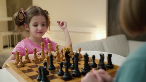 abuela enseñando a jugar al ajedrez a su pequeña nieta en casa