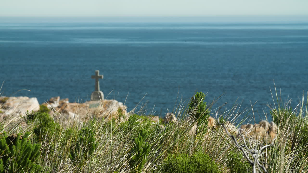Coastal view of grass - shrubs in foreground with gravestone overlooking ocean in background with heatwaves visible