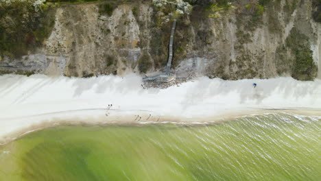 Aerial-view---people-walking-along-the-baltic-sea-at-the-foot-of-a-cliff-in-Wladyslawowo,-Poland