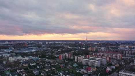 Torre-De-Televisión-De-Riga-En-El-Horizonte-Y-El-Paisaje-Urbano-De-Los-Suburbios,-Vista-Aérea-Con-Cielo-Naranja