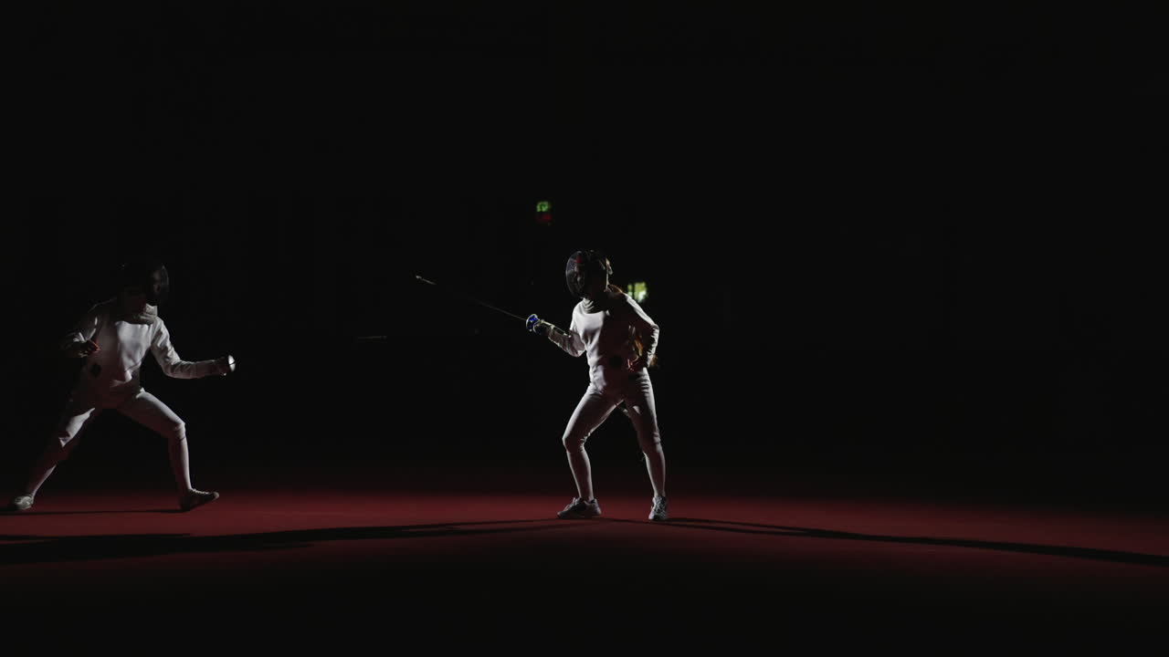 Two fencers in a competition, one in focus and one in shadow