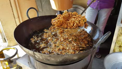 indian onion fritter or locally known as onion pakkoda being fried in a big pan