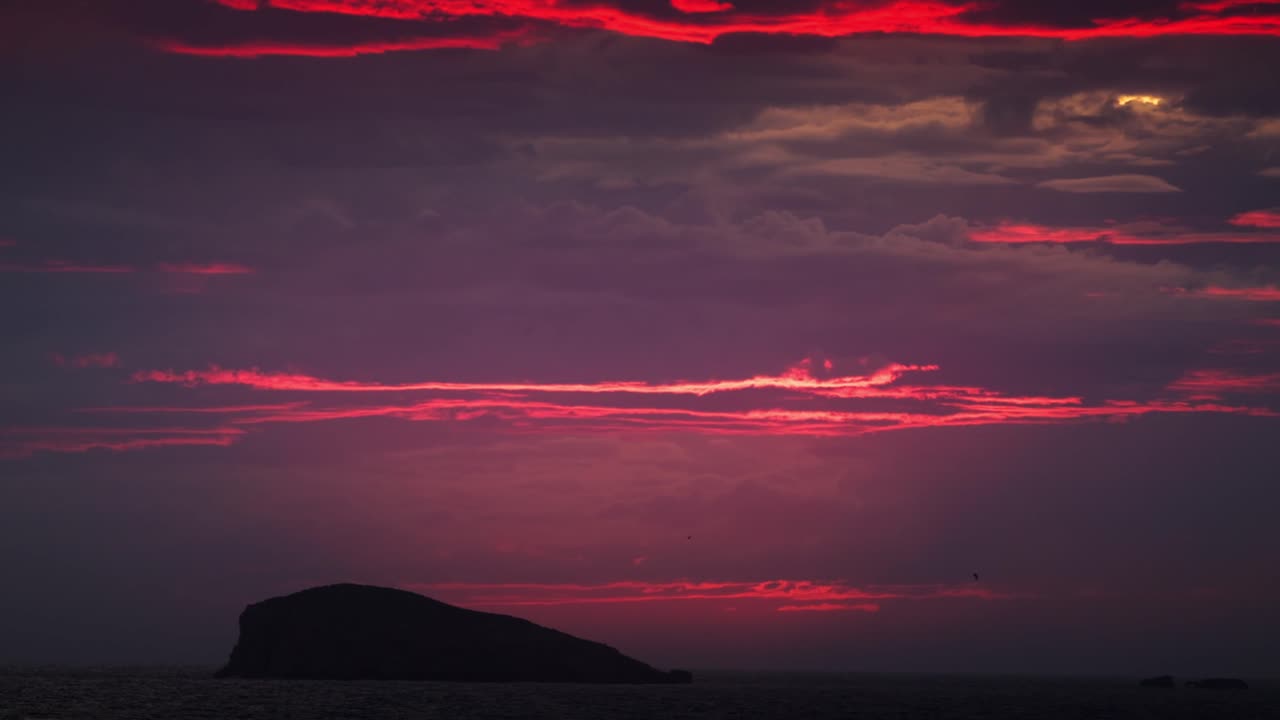 Panorering opad ved Cala Comte på Ibiza, der afslører dramatiske røde og lyserøde solnedgangsskyer over mørket