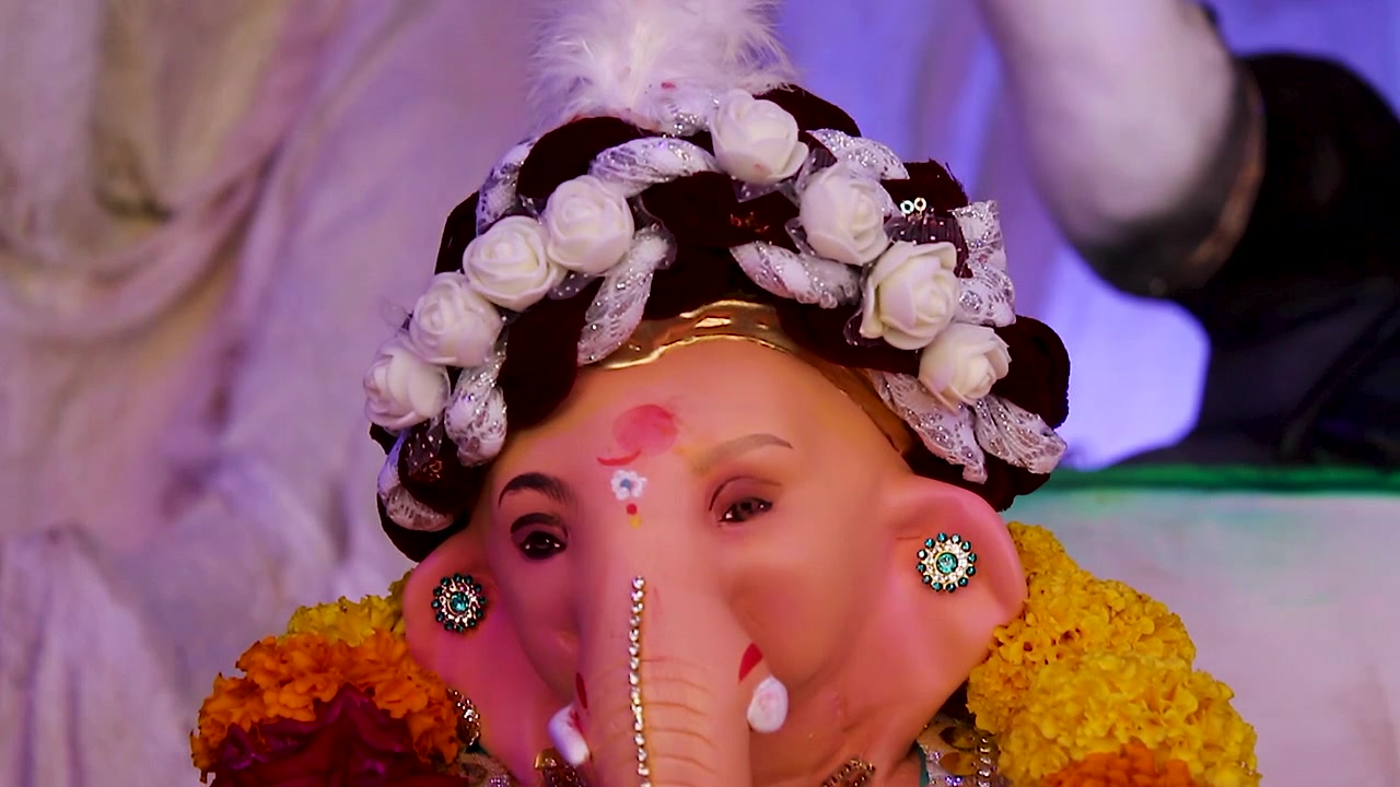 Primo piano del volto della statua di Ganesha che indossa un turbante di rose bianche, fiori di calendula intorno, illuminazione festiva del pandal per la celebrazione di Ganesh Chaturthi in India