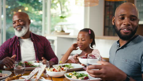 close up of multi-generation family sitting around table serving food for meal at home together
