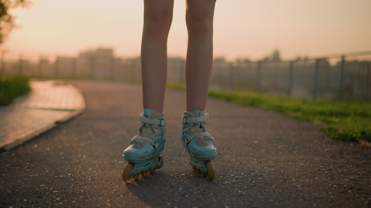 Close-up of lady's legs roller skating outdoors, with legs opening and closing as she balances on pavement during warm evening, sunlight shines from behind, casting shadows on pavement