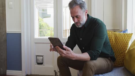 Glücklicher-Kaukasischer-Reifer-Mann,-Der-Im-Wohnzimmer-Sitzt-Und-Ein-Tablet-Benutzt