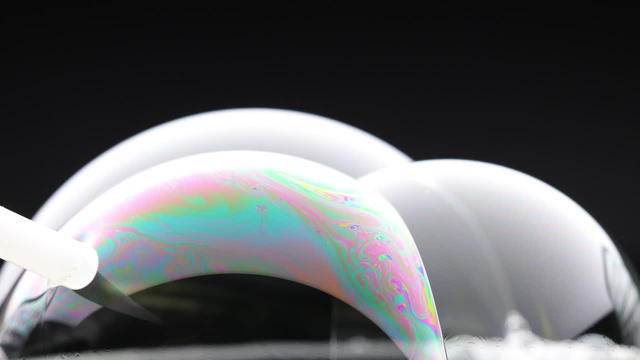 Close-up of soap bubbles displaying vibrant color changes under light. Captures dynamic reflections and fluid motion