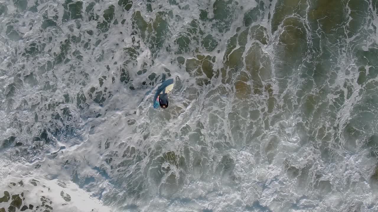 Overhead aerial view of a surfer struggling to get on his board in rough waves