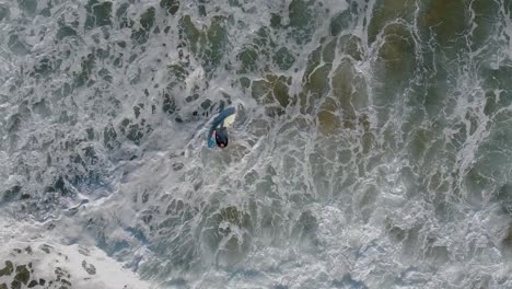 overhead aerial view of a surfer struggling to get on his board in rough waves