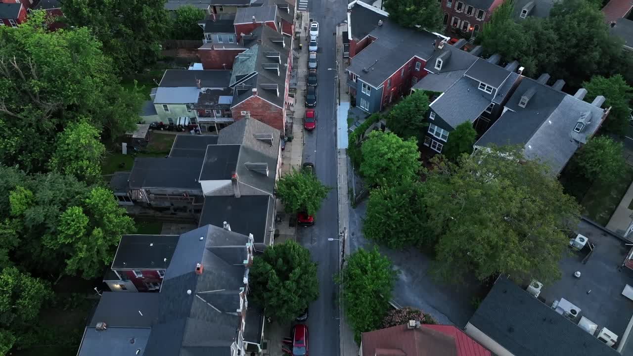 Two-story townhouses and single family homes along suburb road of American Town. Aerial Birds Eye shot. Parking cars along road in Pennsylvania. Green trees in summer