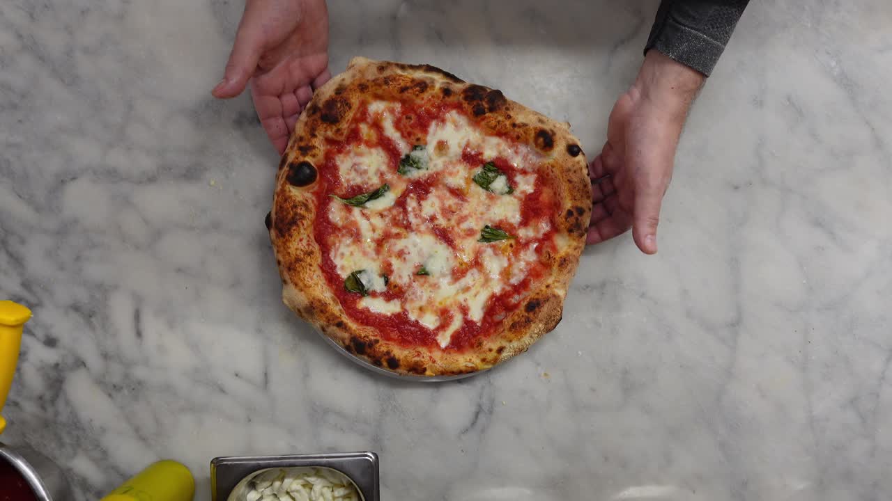 Vista dall'alto di uno chef che mostra una pizza Margherita italiana appena fatta con pomodoro, mozzarella e basilico.