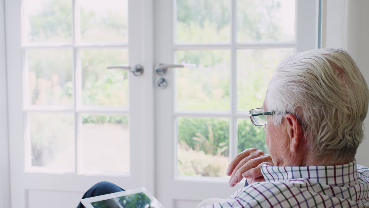 Senior man using tablet computer at home, over shoulder view