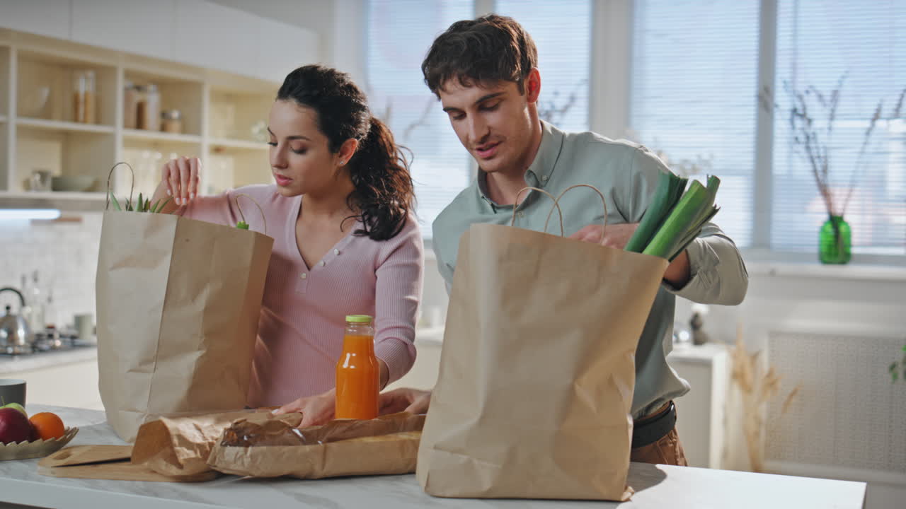 joven familia desempaquetando productos de la tienda de comestibles de pie cocina de cerca.