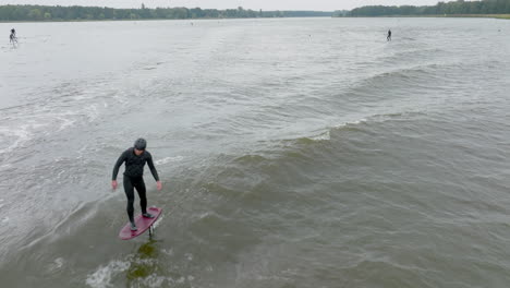 athlete on hydro foil surf in wave with other foil surfer in background close up drone shot