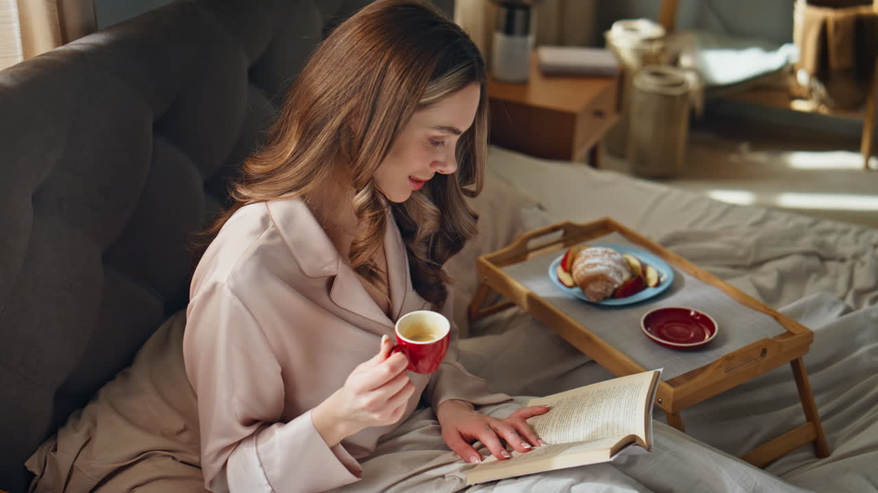 Woman having breakfast in bed while reading a book