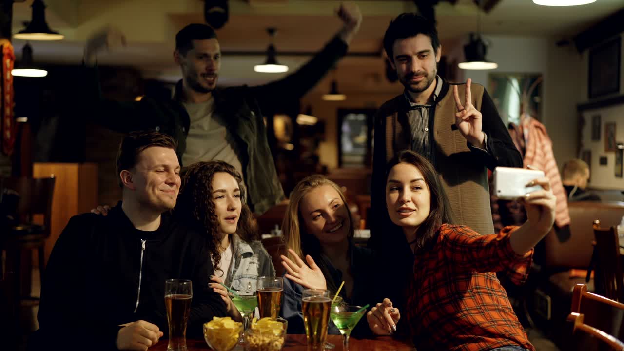 Giovani felici in abiti casual si stanno scattando un selfie in un bar. Stanno posando, facendo facce buffe, ridendo e gesticolando. Concetto di foto divertenti per bei ricordi.