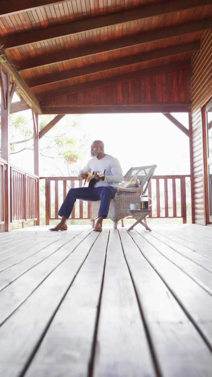Vertikal video af ældre afroamerikansk mand, der tilbringer tid i bjælkehytte og spiller guitar