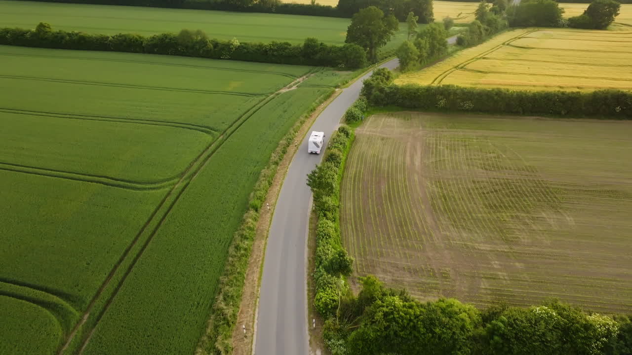 Aerial view following a EV RV driving in middle of blooming fields, golden hour