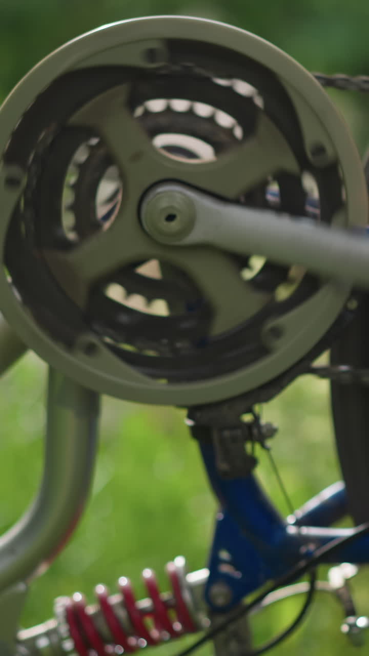 primer plano del pedal de la bicicleta girando a mano hacia atrás, haciendo que la rueda gire rápidamente, el enfoque está en el sistema de engranajes y la cadena, con el fondo con vegetación borrosa