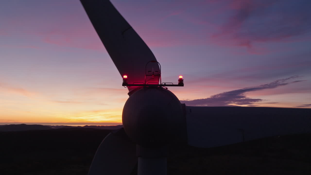 Primo piano allargato di turbine eoliche che si stagliano sulle colline al tramonto, creando uno scenario di energia.