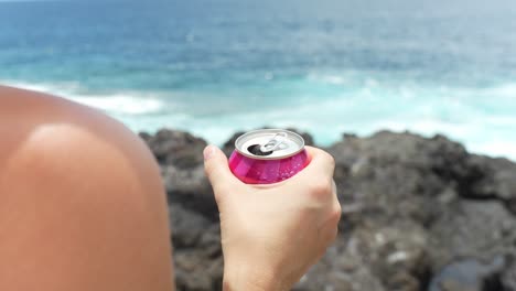 Woman-holding-can-in-her-hand-with-cold-drink-near-ocean-coastline