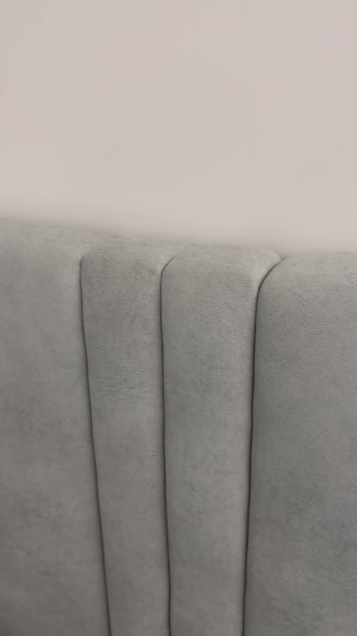 Vertical close up of grey fabric bed headboard against plain wall