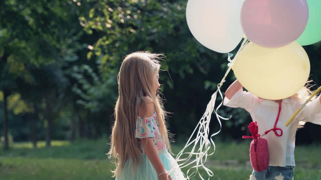 Two cute girls with balloons and a butterfly net are playing a game of rock-paper-scissors on a holiday in the park. Soap bubbles in nature
