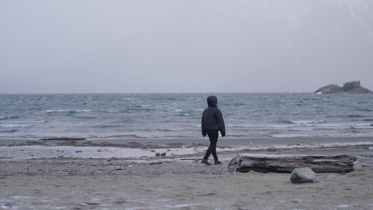 Woman walking by frozen lake shore under gray skies, emotional travel, Bariloche, Argentina