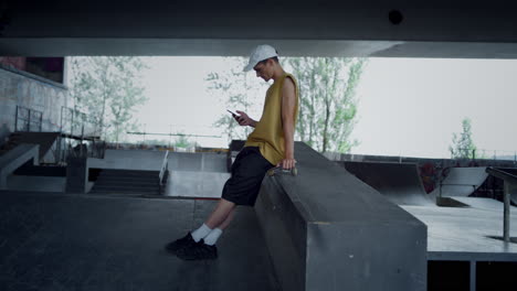 Lässiger-Teenager,-Der-Sich-Mit-Dem-Smartphone-Entspannt-Und-Auf-Dem-Skateboard-Im-Skatepark-Sitzt.