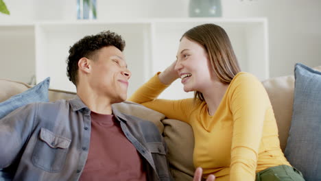 happy diverse couple sitting on sofa talking and laughing at home, in slow motion