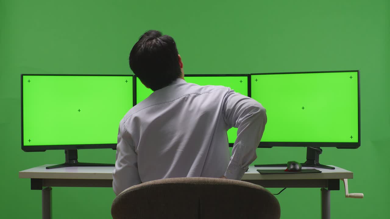 hombre de negocios con dolor de espalda frente a un monitor triple