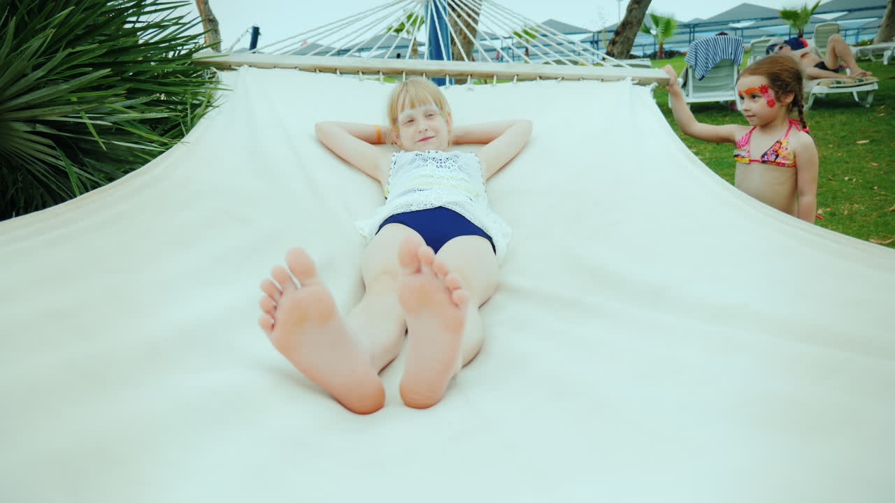 una niña sacude a su hermana mayor en una hamaca divirtiéndose durante las vacaciones de verano