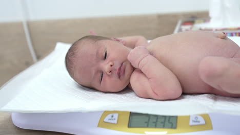 naked child lying on the electronic scales and hiccupping. cute newborn baby being weighed in maternity unit in the hospital.