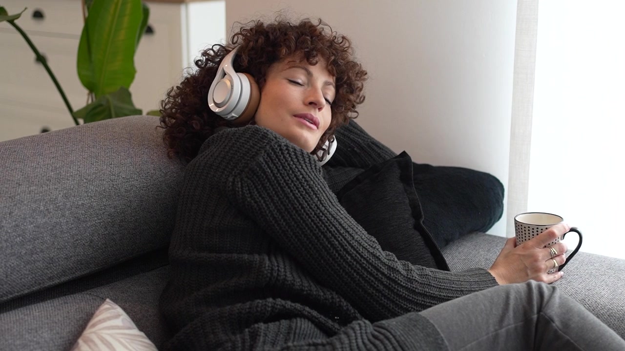En kvinde slapper af derhjemme og finder glæde ved at lytte til musik, mens hun nyder en varm drik.