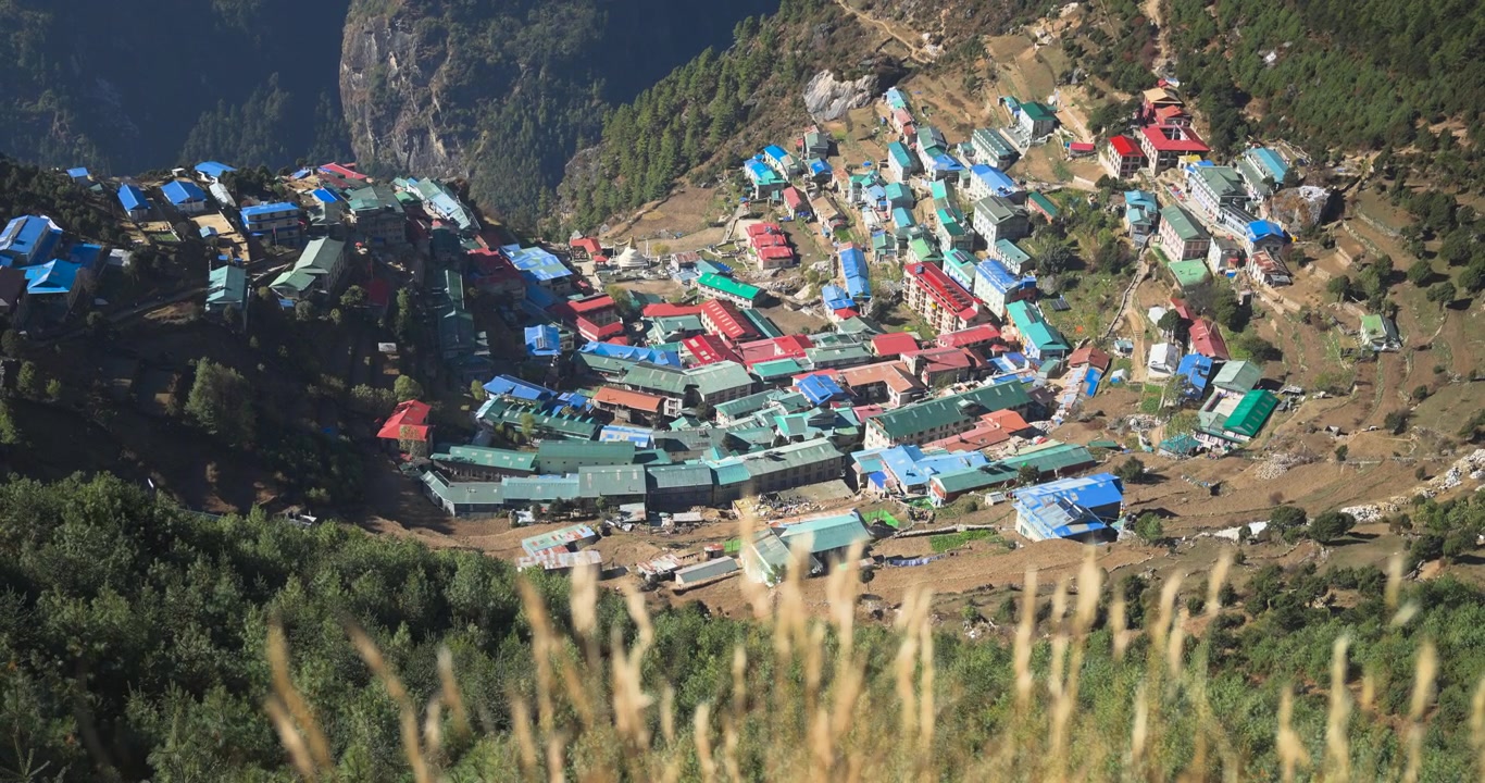 Namche Bazaar, Everest Region, Nepal, static top-down shot of colorful building roofs and terraces built along a steep grassy hill cliffside.